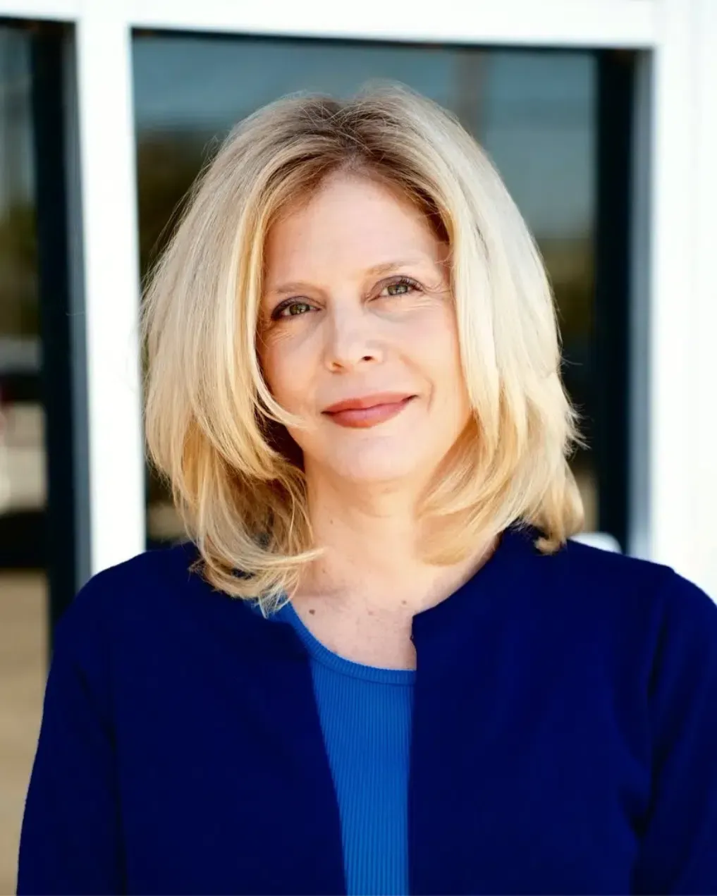 A woman in a blue jacket and blue shirt is standing in front of a building.