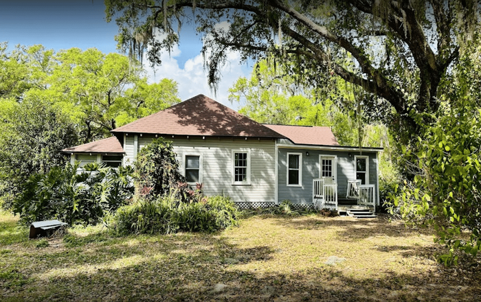 A white house with a red roof is surrounded by trees and grass.