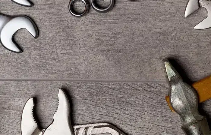 A hammer , pliers , wrenches and scissors are on a wooden table.