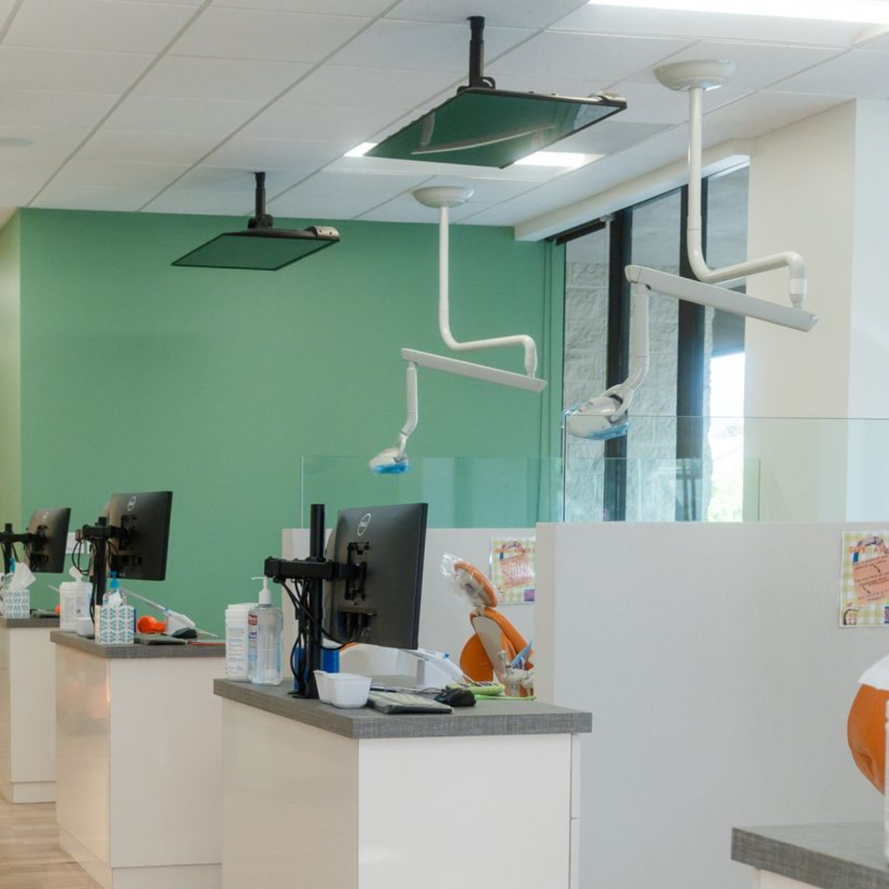 Dental office with workstations and overhead lights; green wall in background.