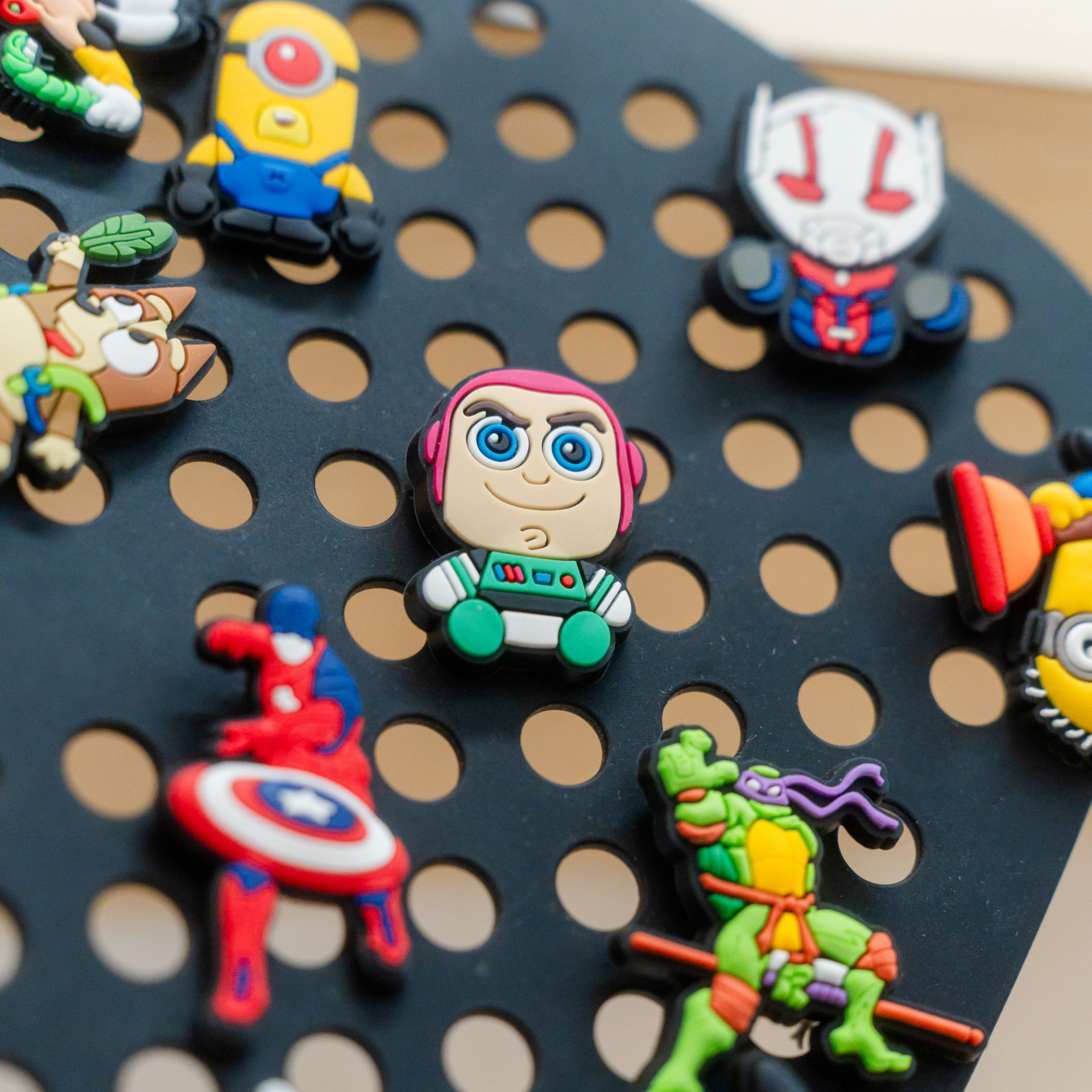 Toy story character Buzz Lightyear charm surrounded by other cartoon charms on a black, perforated surface.
