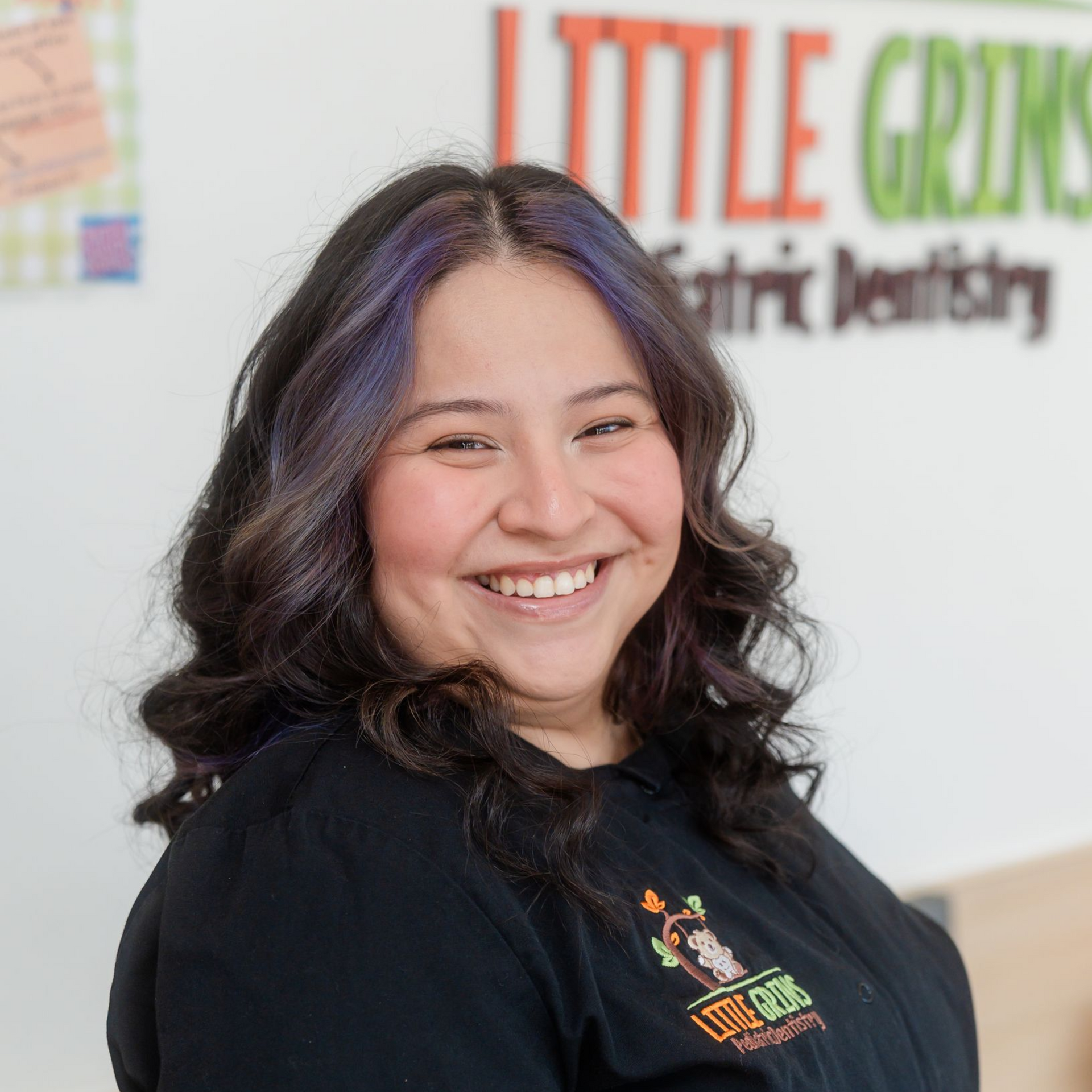 Woman with purple-streaked hair, smiling in front of a 