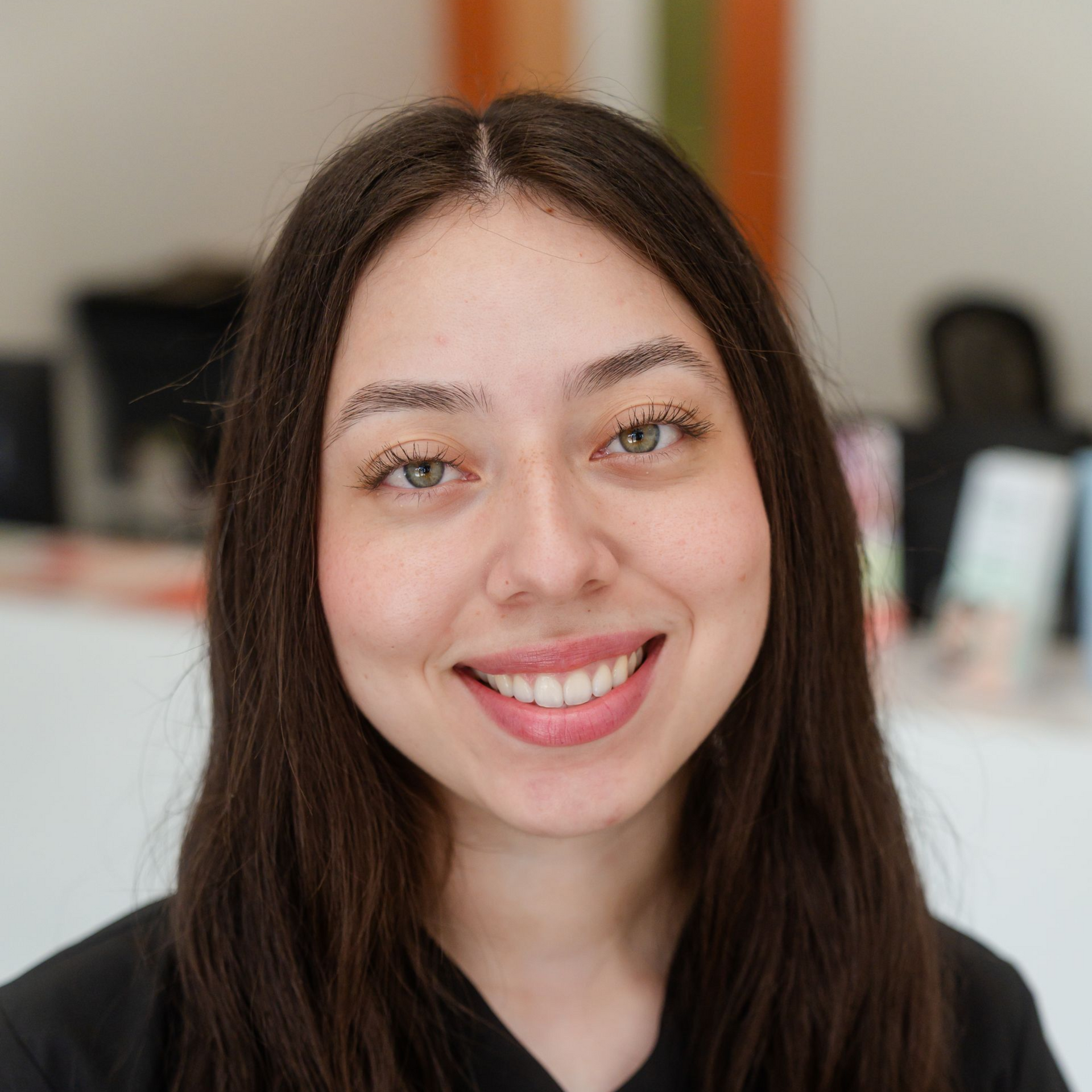 Woman with brown hair and light eyes smiling, in an office setting.