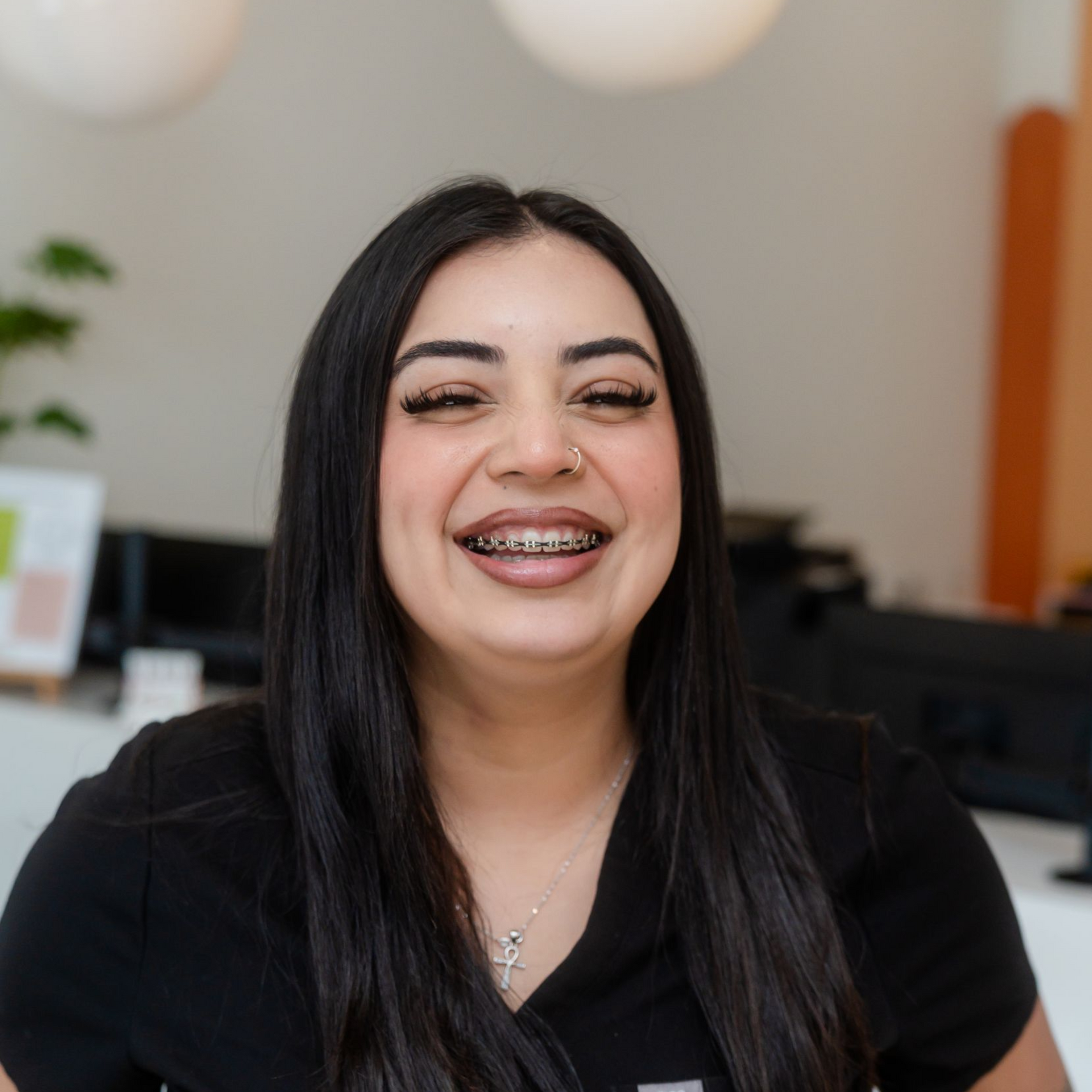 Woman smiling, wearing braces, black shirt. Indoors, bright setting.