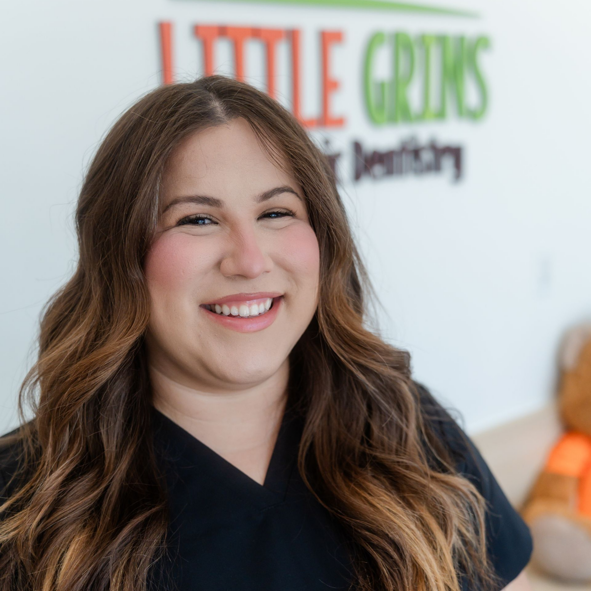 Woman with brown hair smiles, standing in a children's dental office, the logo 
