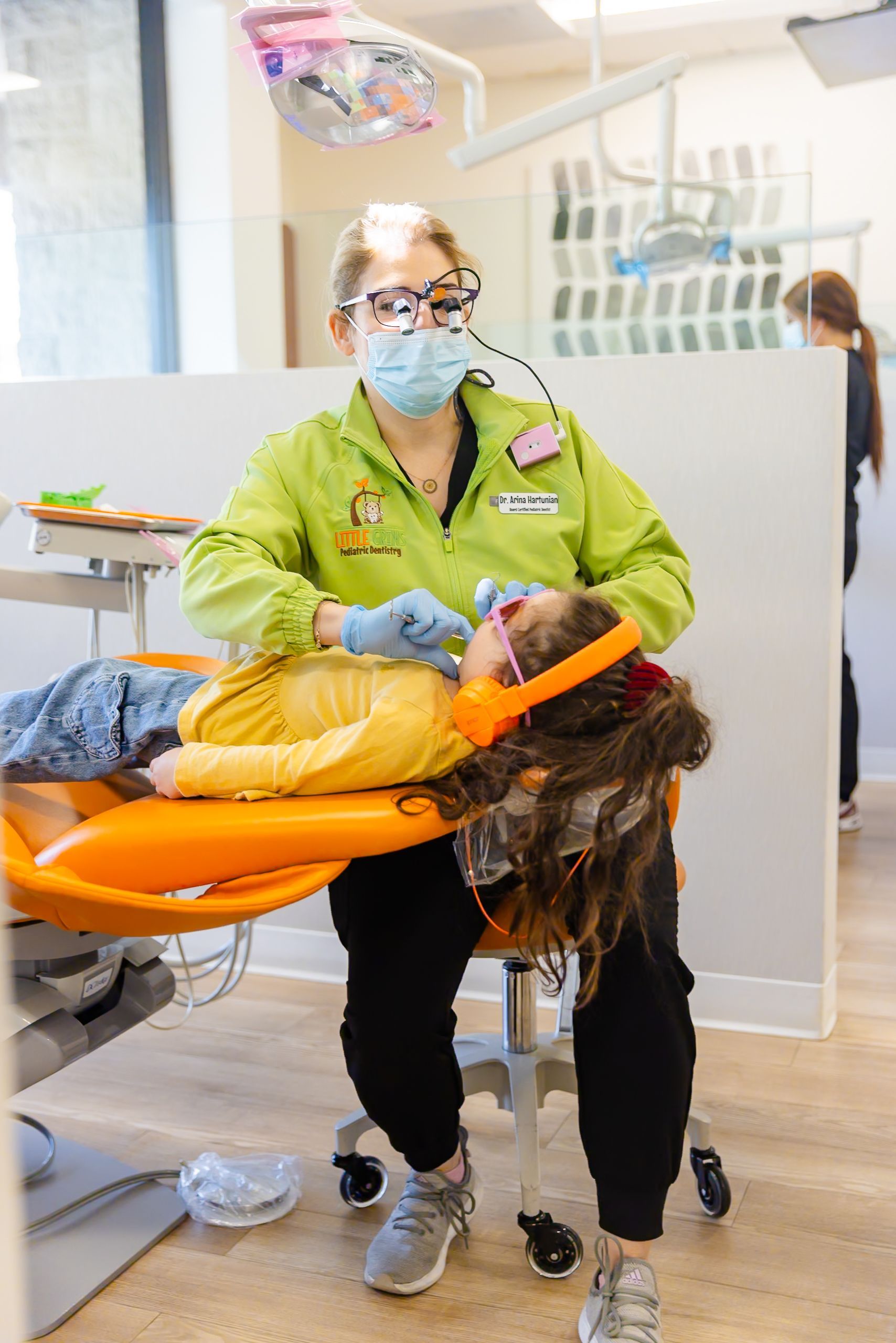 Dentist examining a child's teeth while held by a person in a dental chair.