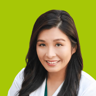 Woman with dark hair smiling, wearing a white coat and green top, against a green background.