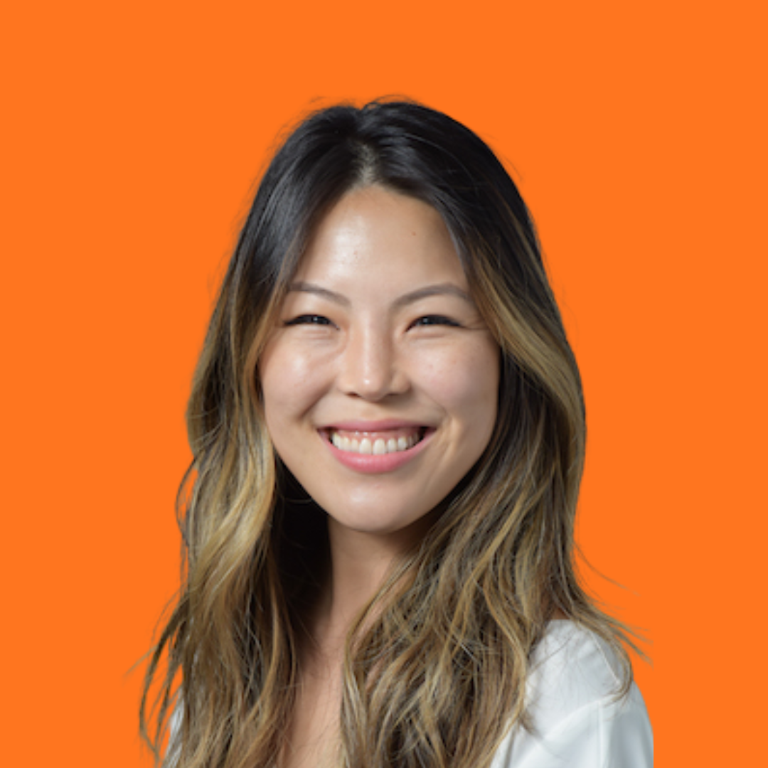 Woman with long brown hair smiling against an orange background.