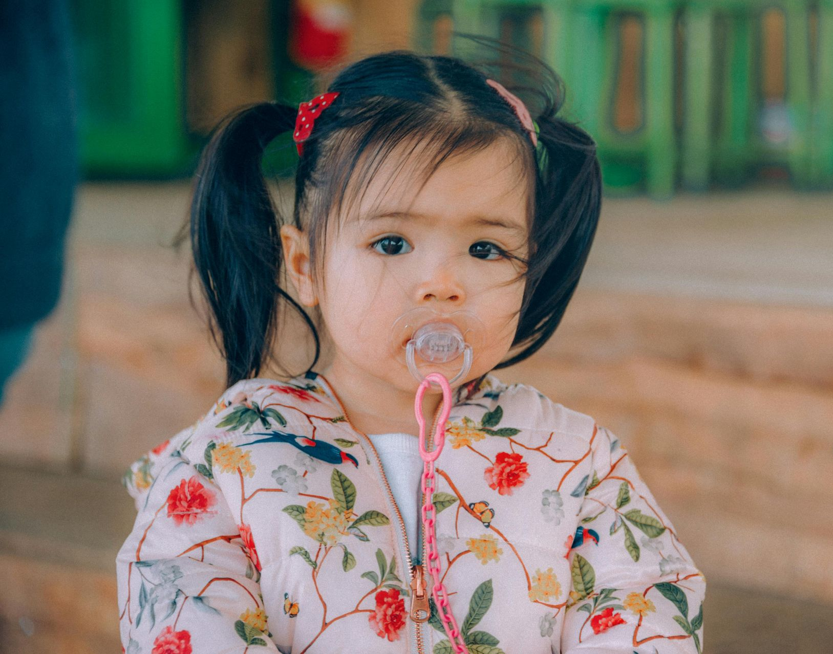 Young child with dark hair in pigtails blowing a bubble. Wearing a floral jacket and holding bubble wand.