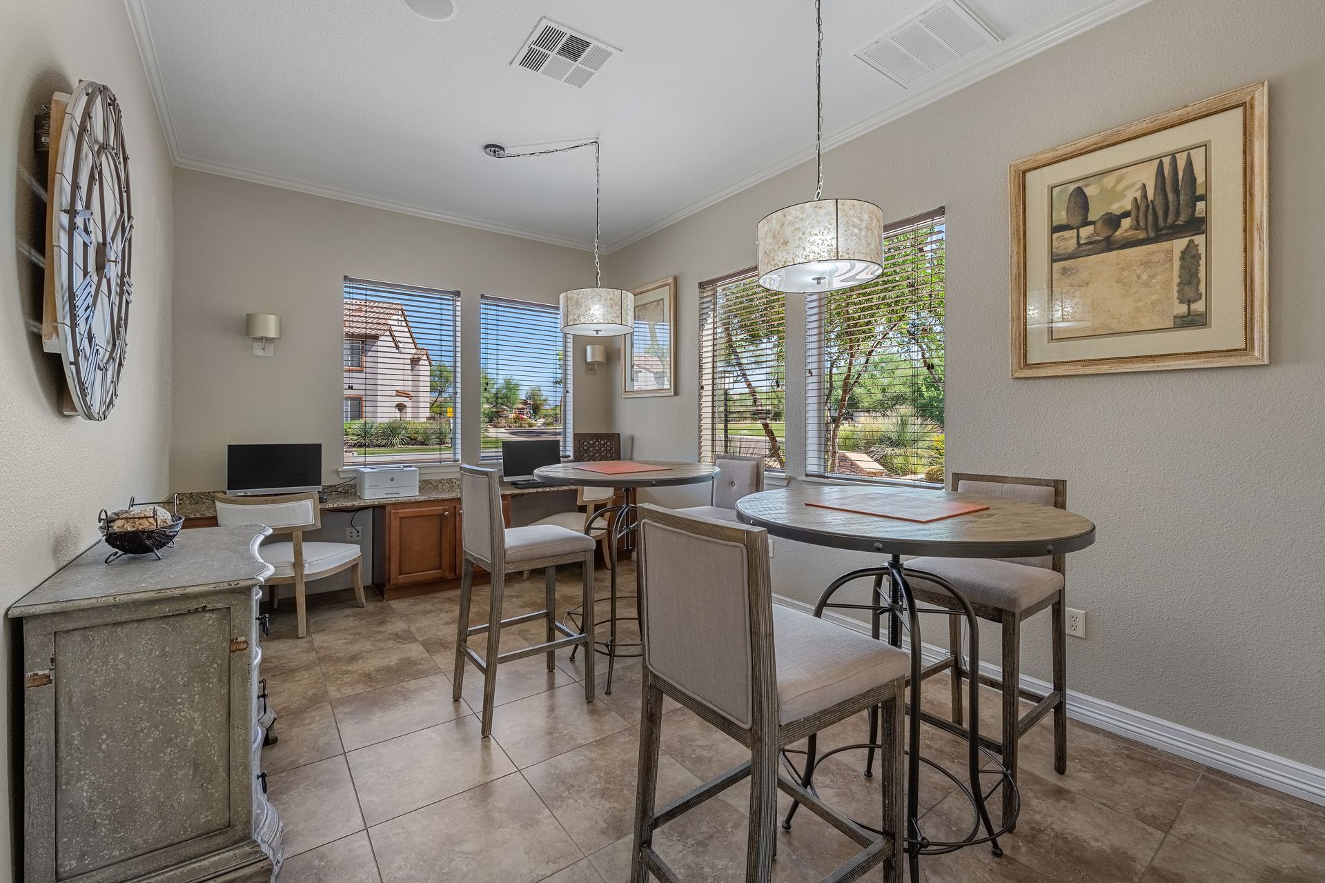 Bright dining room with round table, chairs, pendant lights, and large windows overlooking a green patio.