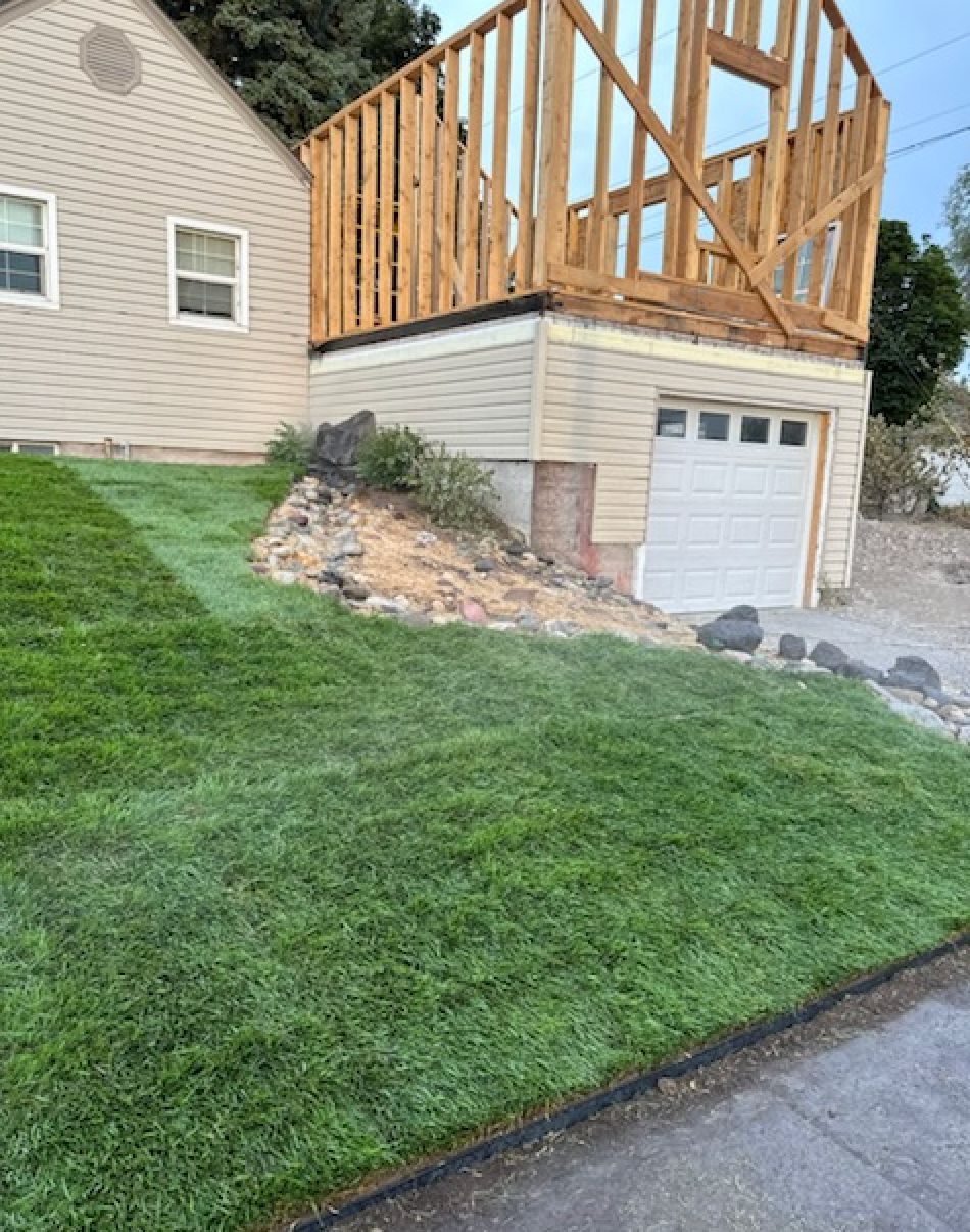 A beige house with a garage underneath, featuring exposed wooden framing for a second-story addition above the garage.