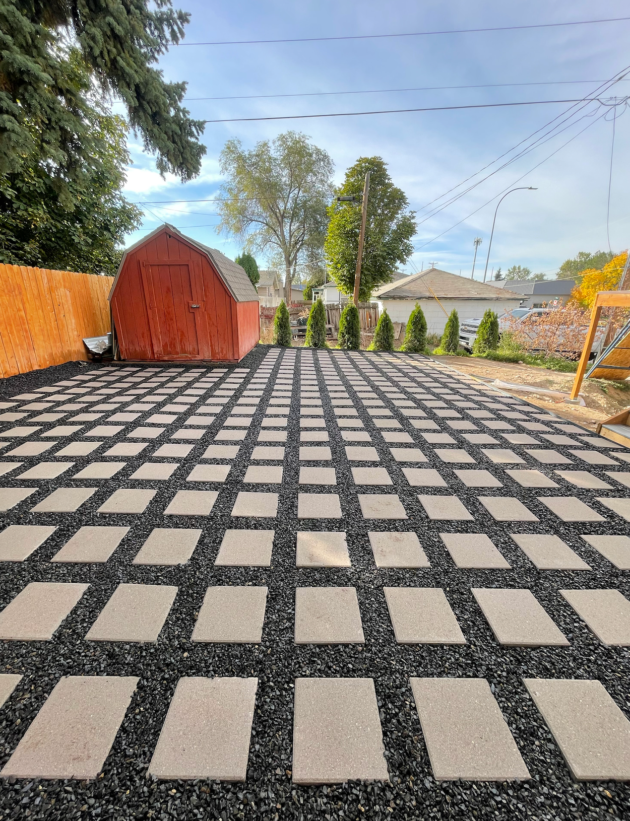 A backyard patio featuring a grid pattern of rectangular concrete pavers surrounded by dark gray crushed gravel.