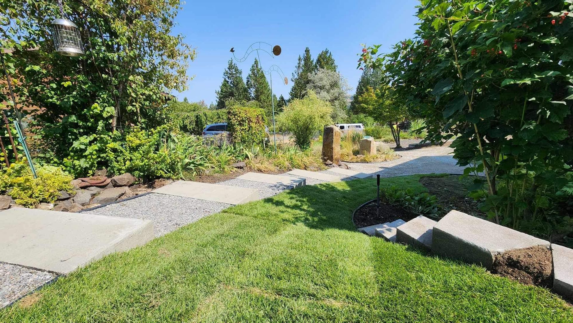 Green grass, a stone path, and garden leading towards trees and a sunny sky.