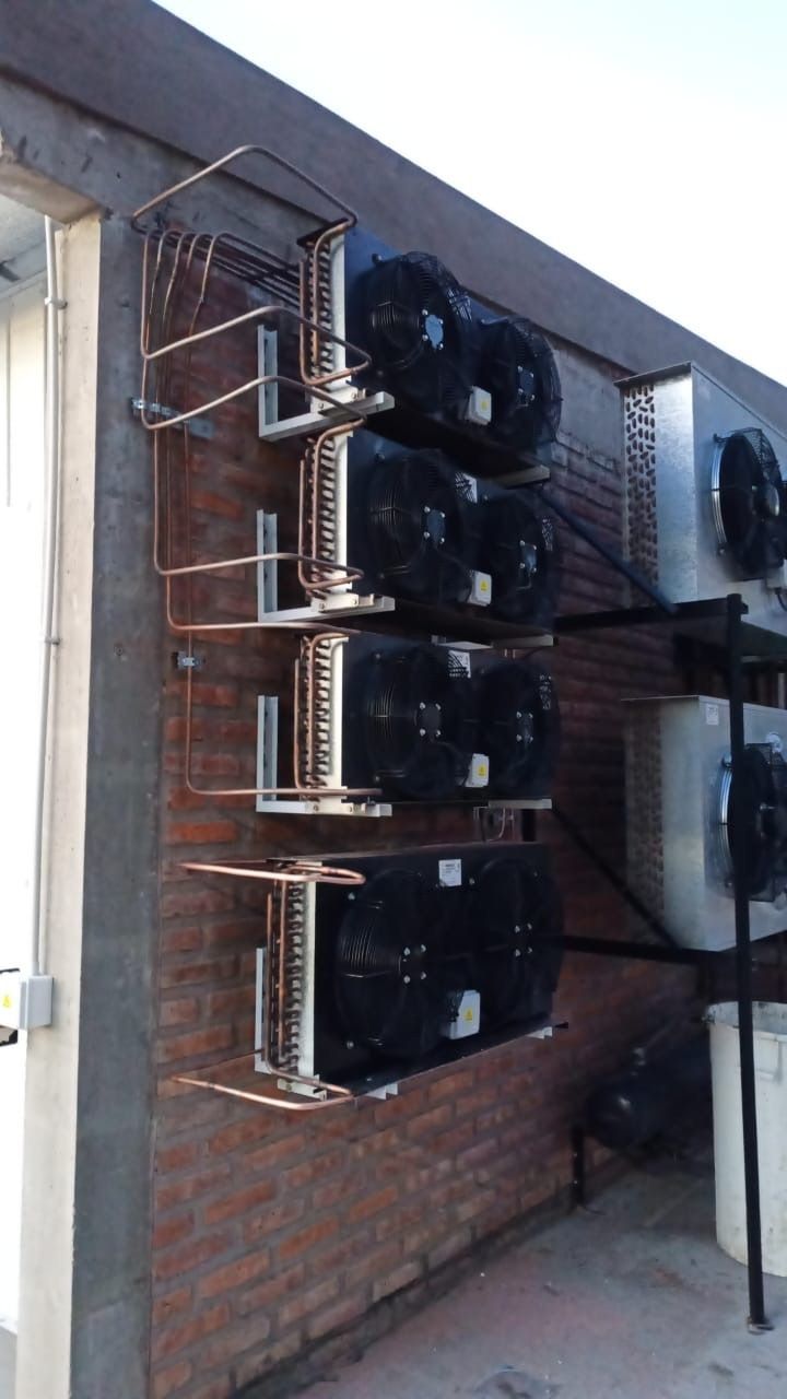 Cuatro unidades de aire acondicionado industriales montadas verticalmente en una pared exterior de ladrillo