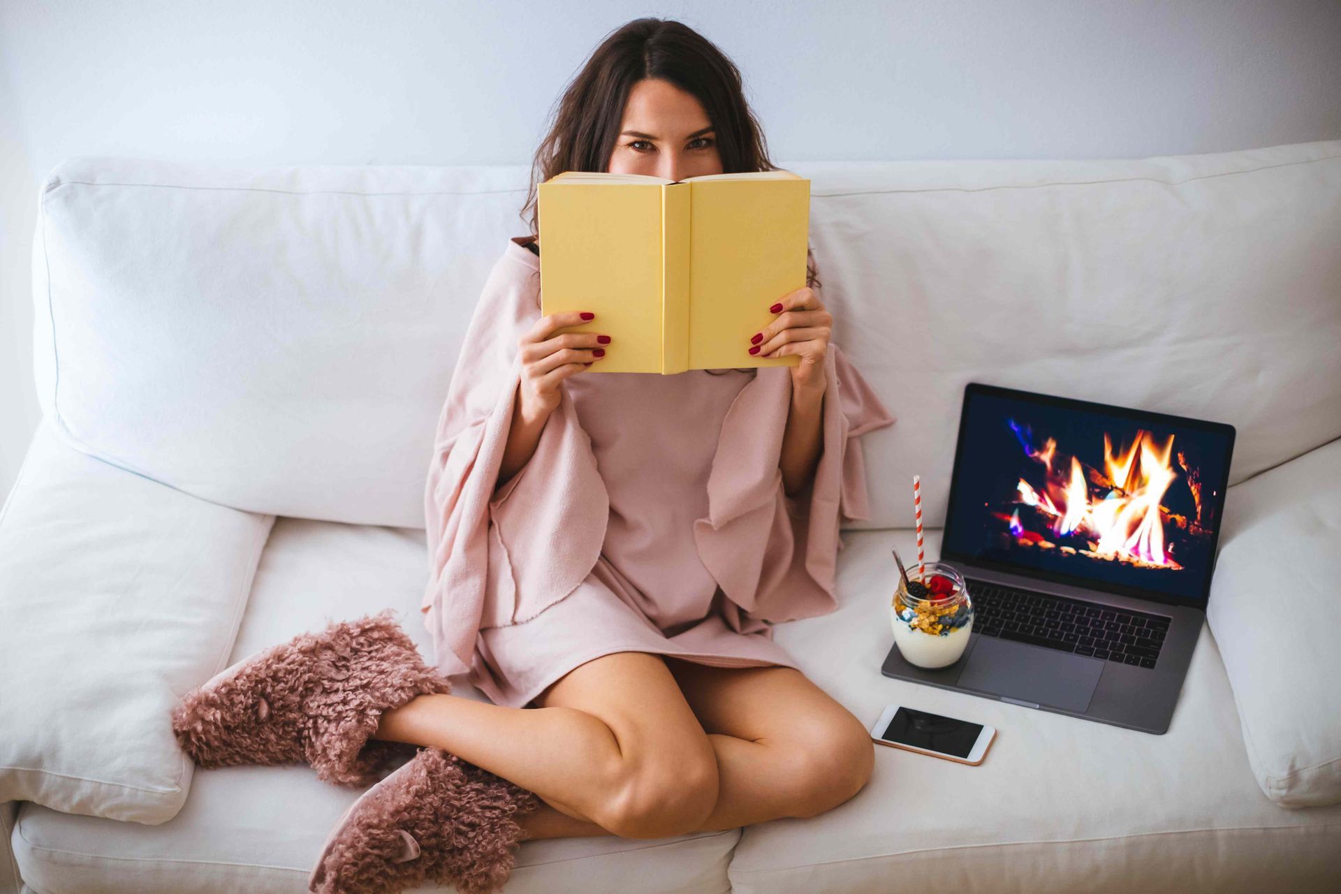 Woman with book on couch fireplace on her laptop