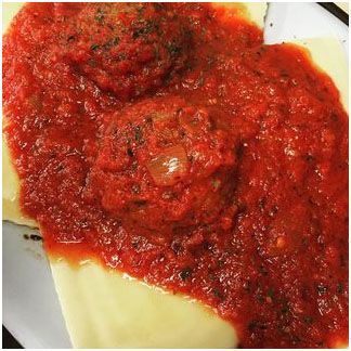 A close up of a plate of ravioli with tomato sauce and meatballs