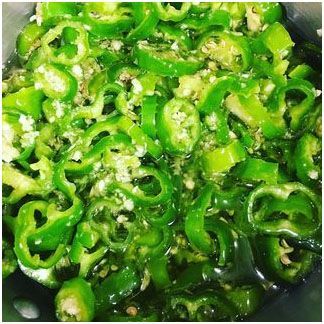 A close up of long hot peppers and garlic in a pan