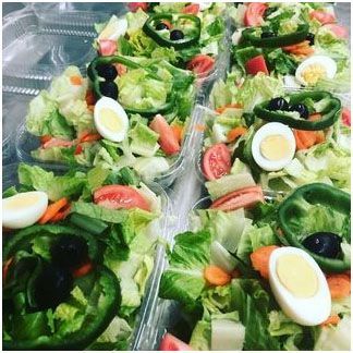 A salad with lettuce, eggs, peppers, carrots and olives in plastic containers.