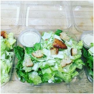 A caesar salad in a plastic container on a wooden table