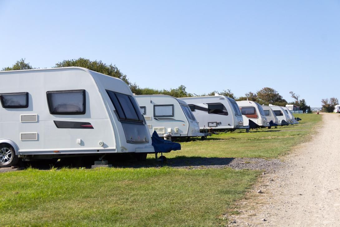 A row of caravans are parked in a grassy field.