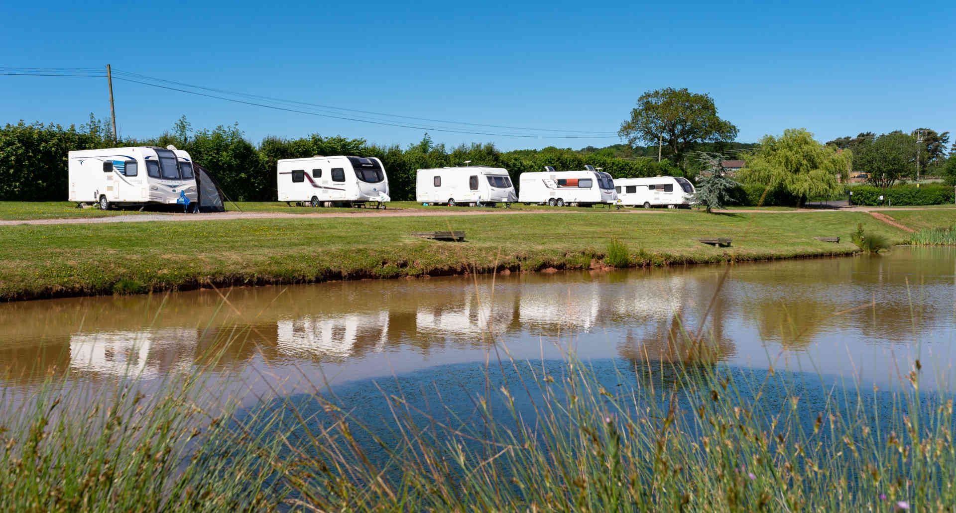 A row of rvs are parked next to a body of water.
