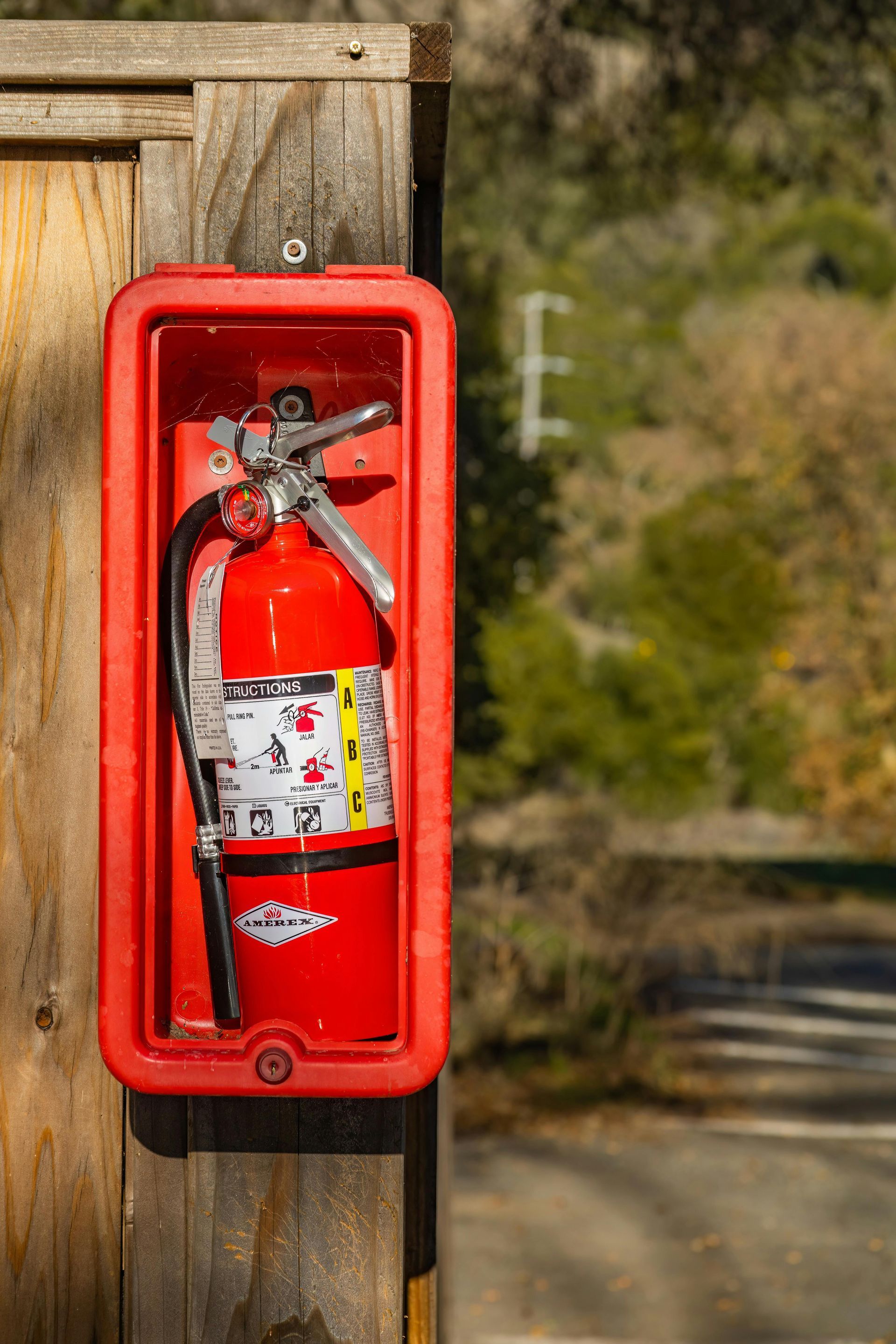 A red fire extinguisher is hanging on a wooden fence.