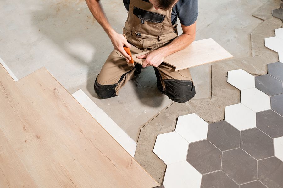 A man is kneeling on the floor while installing a wooden floor.