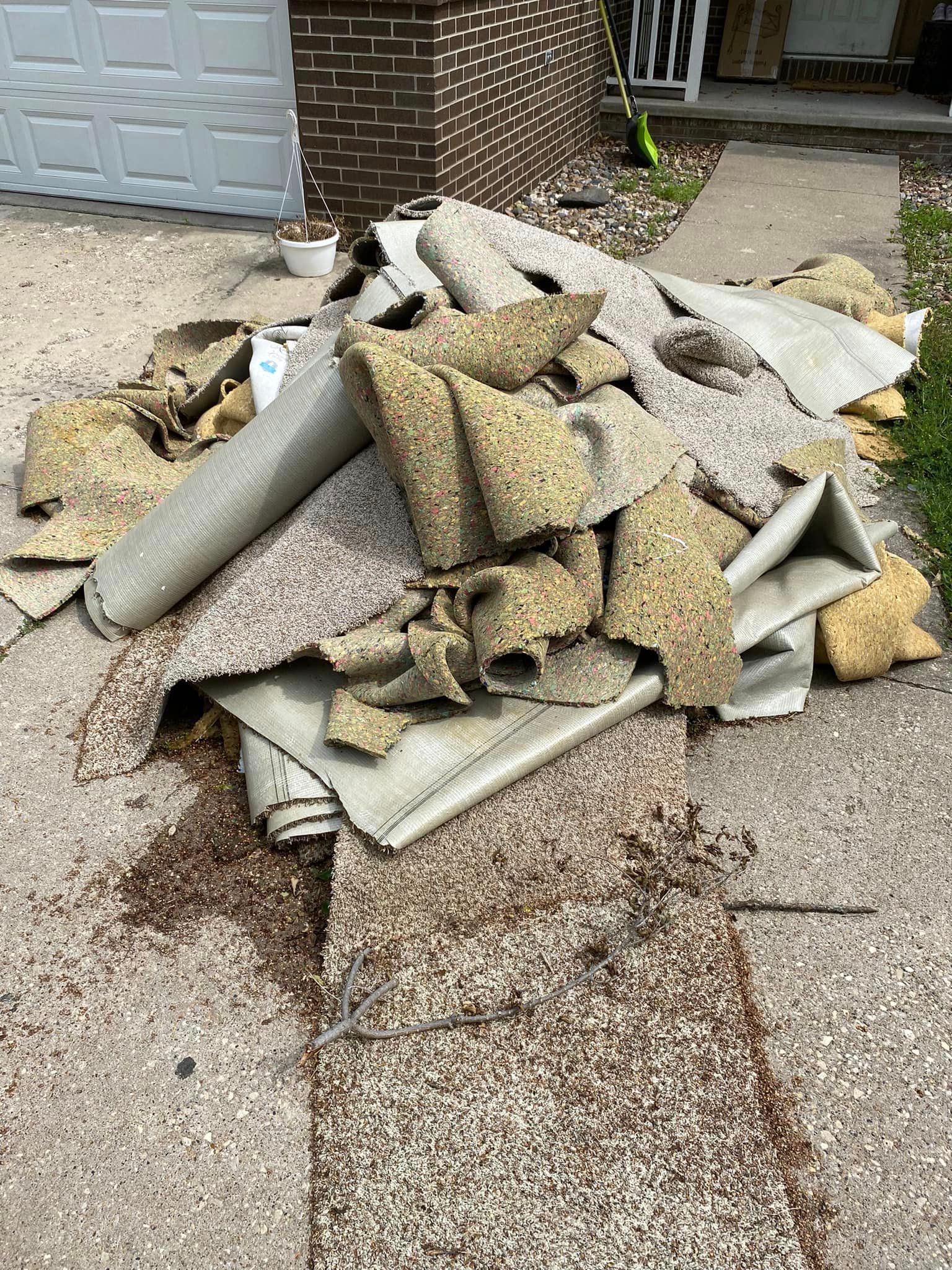 A pile of carpet is sitting on the sidewalk in front of a garage door.