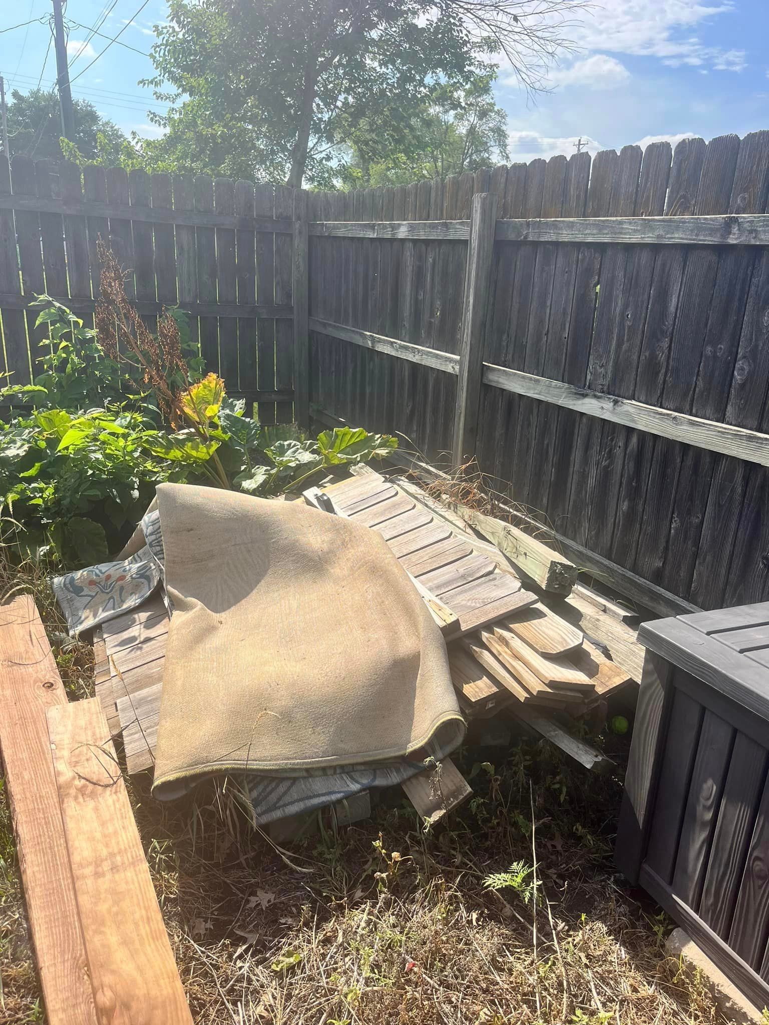 A pile of wood is sitting on the ground in front of a wooden fence.