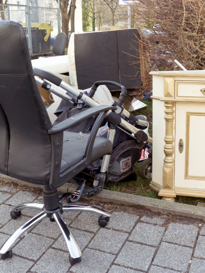 A black office chair is sitting on a sidewalk next to a stroller.