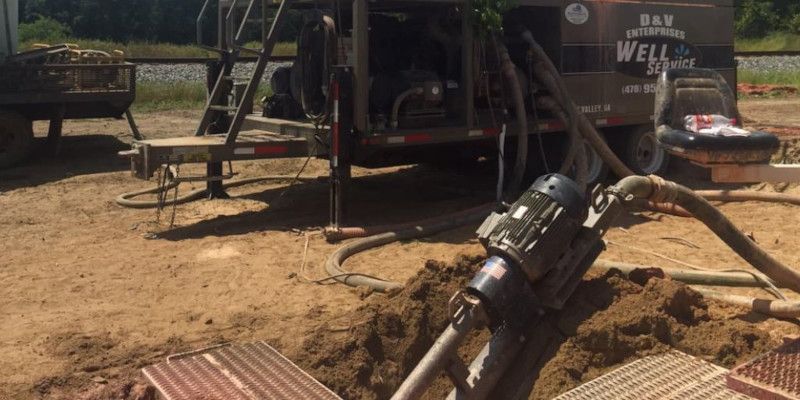 A truck is sitting in the dirt next to a well pump.