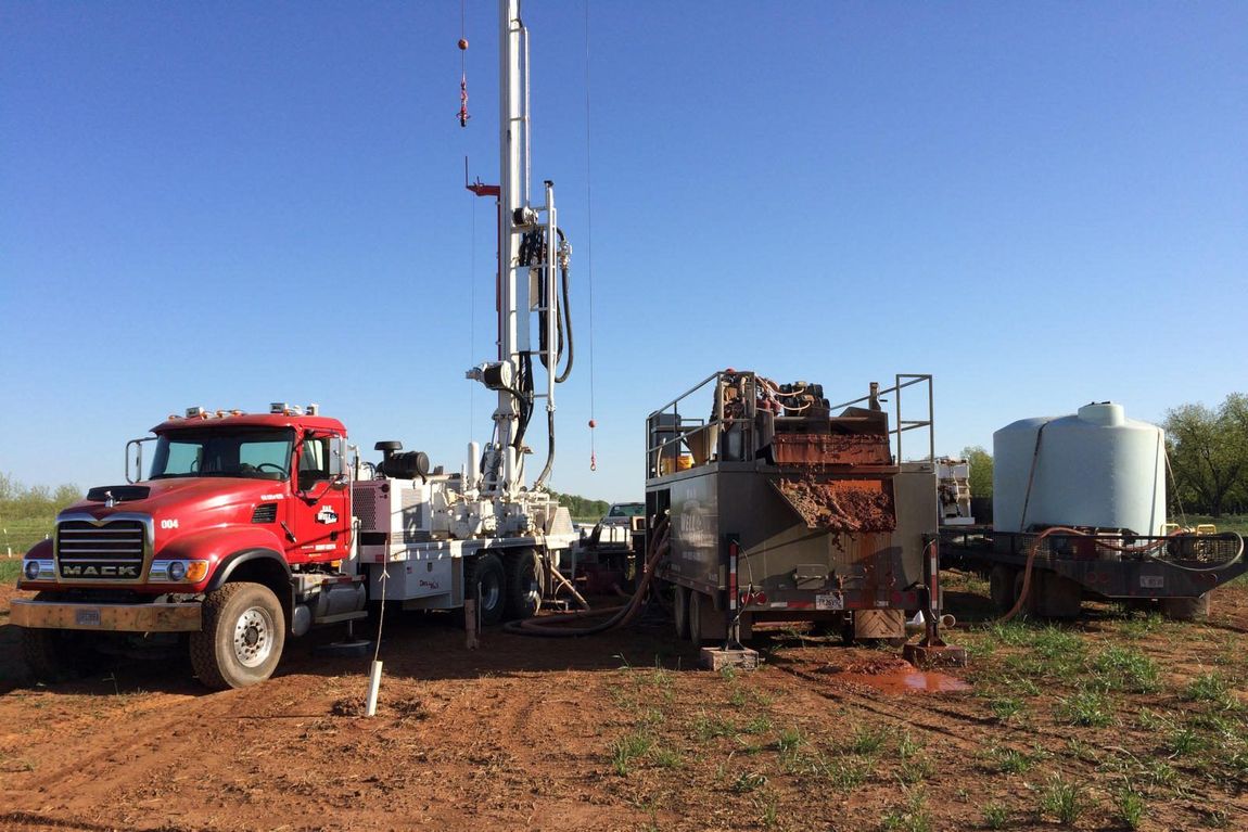 A red truck is parked next to a white truck in a dirt field.