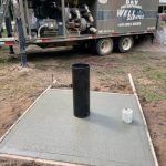 A black cylinder is sitting on top of a concrete slab next to a truck.