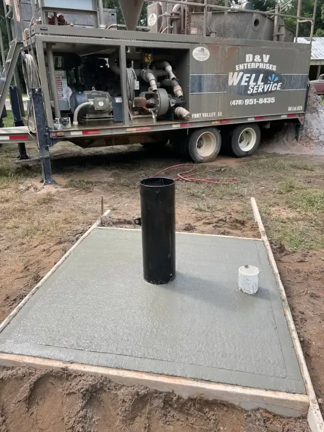 A well pump is sitting on top of a concrete platform next to a truck.