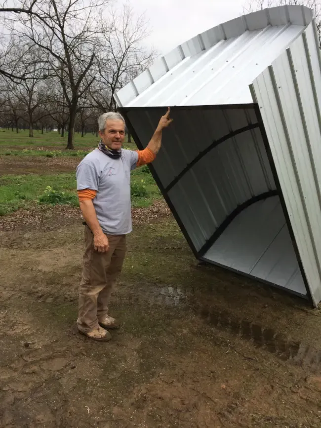 A man is standing next to a shed that has fallen over.