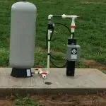 A water pump is sitting on top of a concrete platform in the grass.