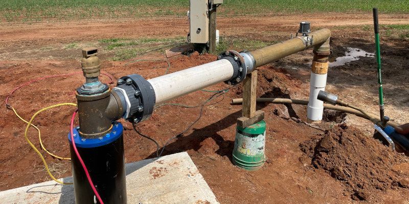 A water pump is sitting in the dirt next to a pipe.