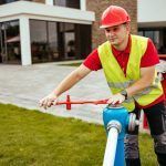 A man wearing a hard hat and safety vest is working on a fire hydrant.