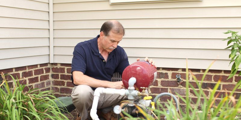 A man is working on a water pump outside of a house.