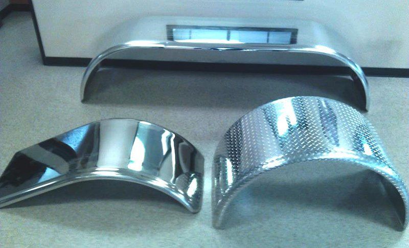 Three chrome fenders are sitting on a carpeted floor