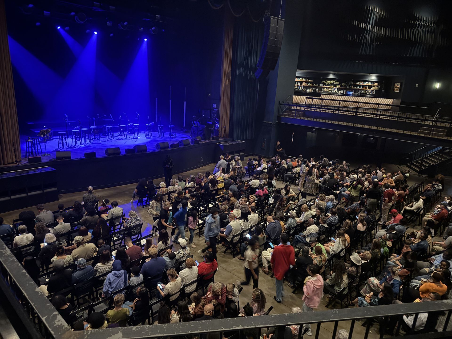 Large theater with stage bathed in blue light. Orchestra on stage, audience in seats below.