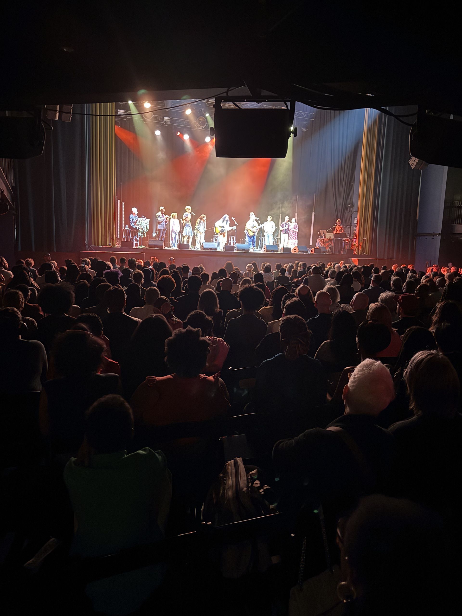 Audience watches a performance on a brightly lit stage in a theater.