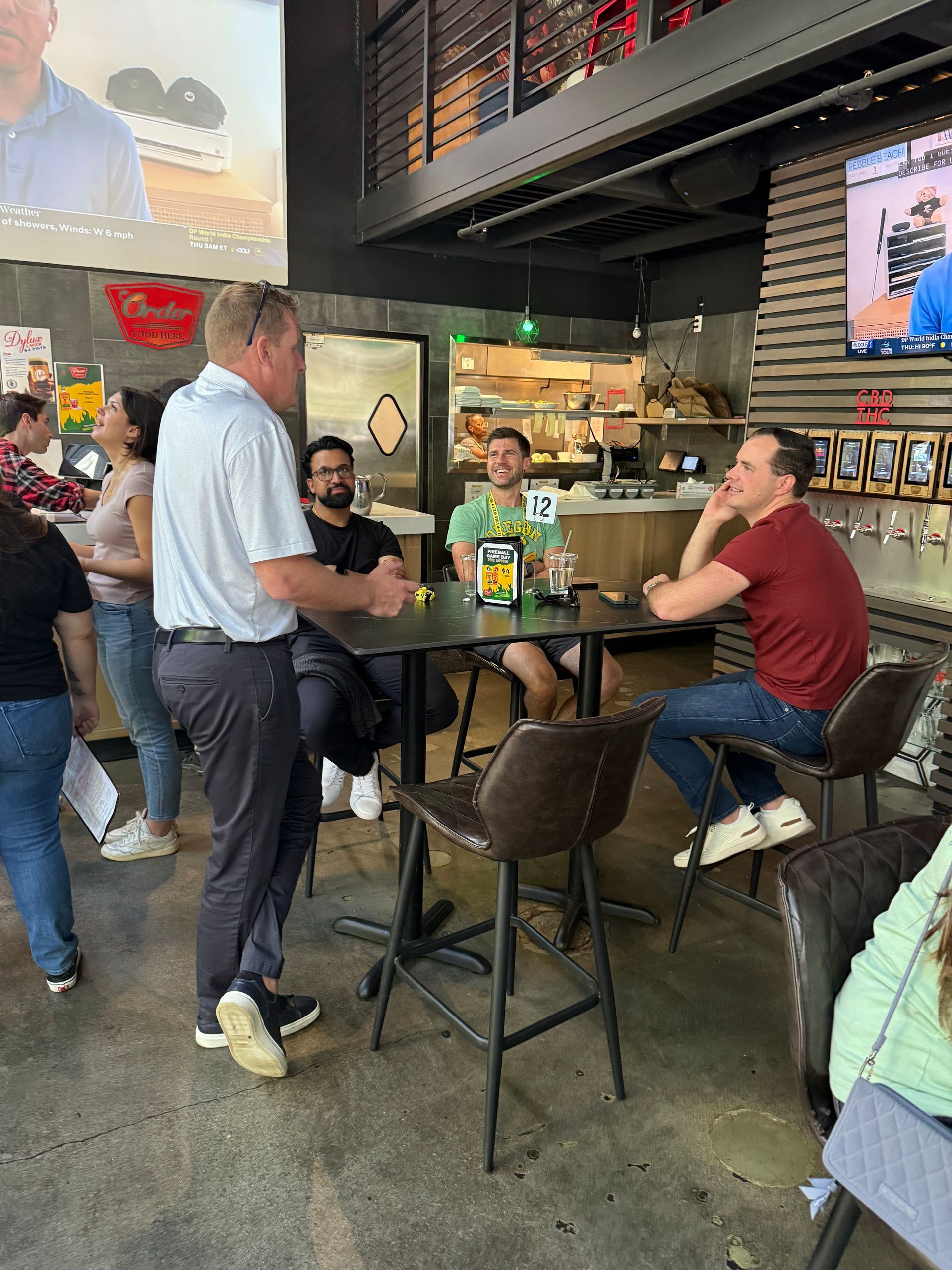 People at tables inside a restaurant. One man in light blue shirt talks, others sit and listen.
