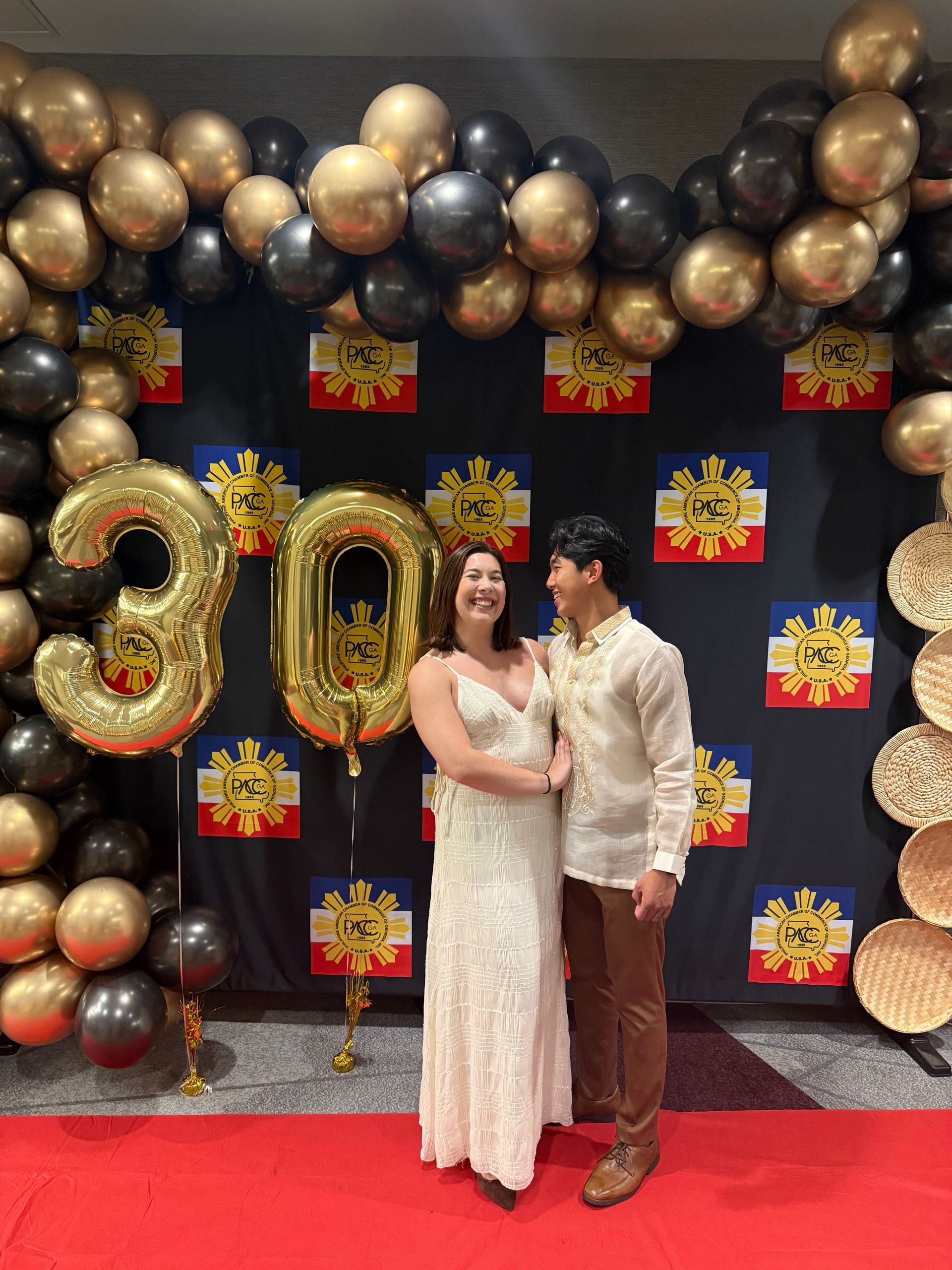 Couple posing at a party with gold/black balloons and 30 balloon. Red carpet, Philippine flag backdrop.