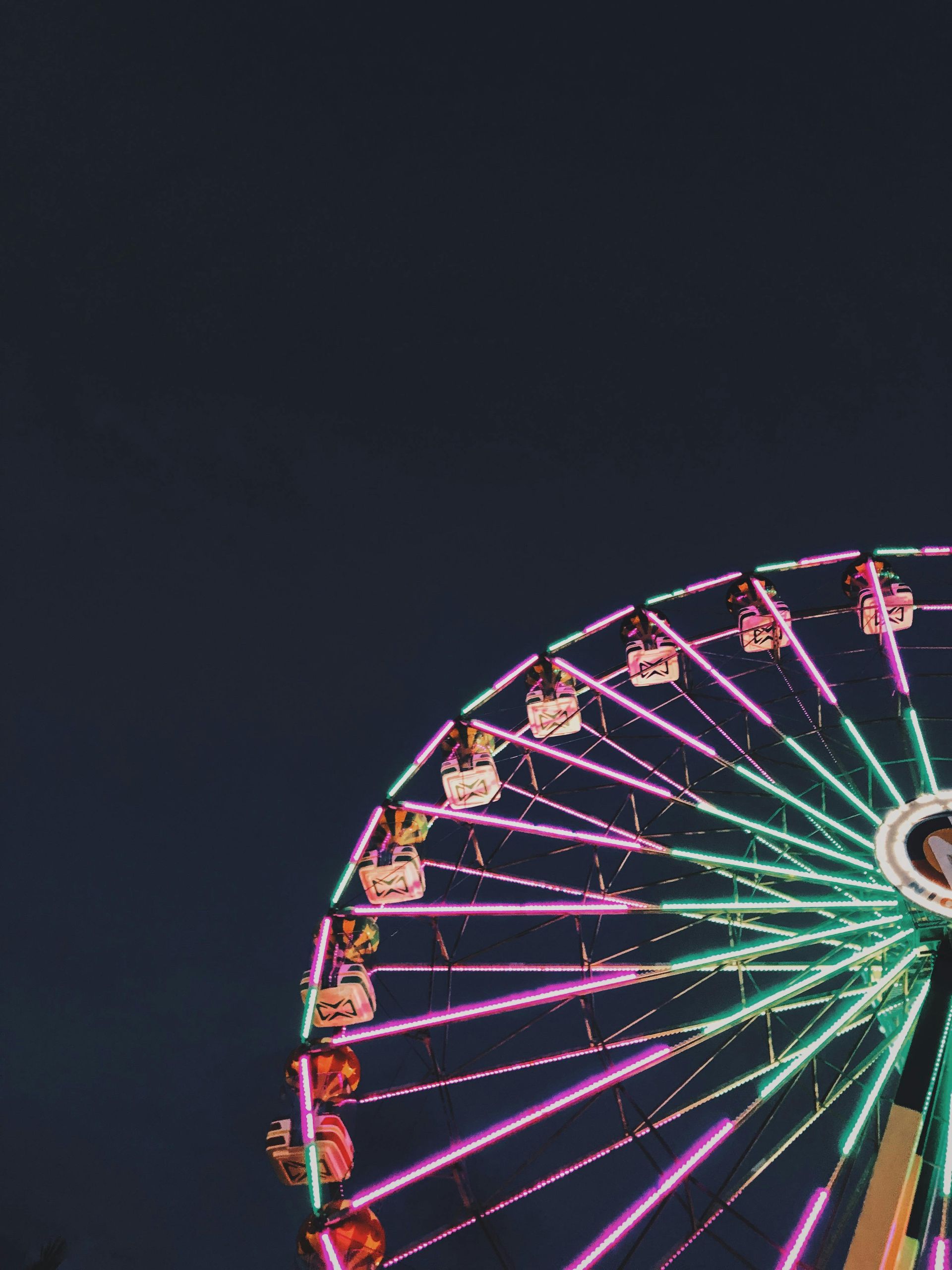 Ferris wheel with pink and green lights against a dark blue sky.