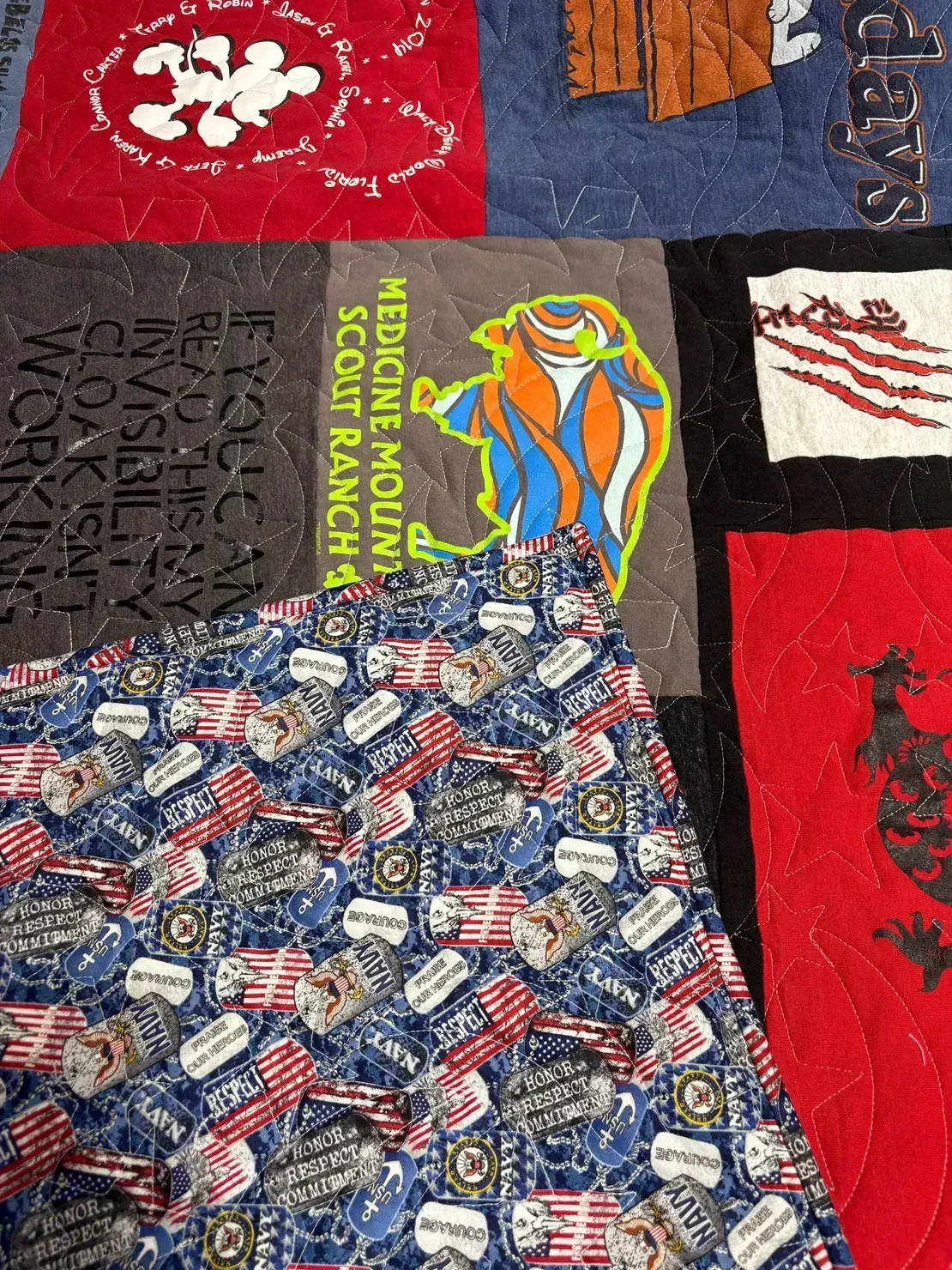 A patchwork quilt featuring various patterned squares, including a Medicine Mountain Scout Ranch logo and patriotic motifs.