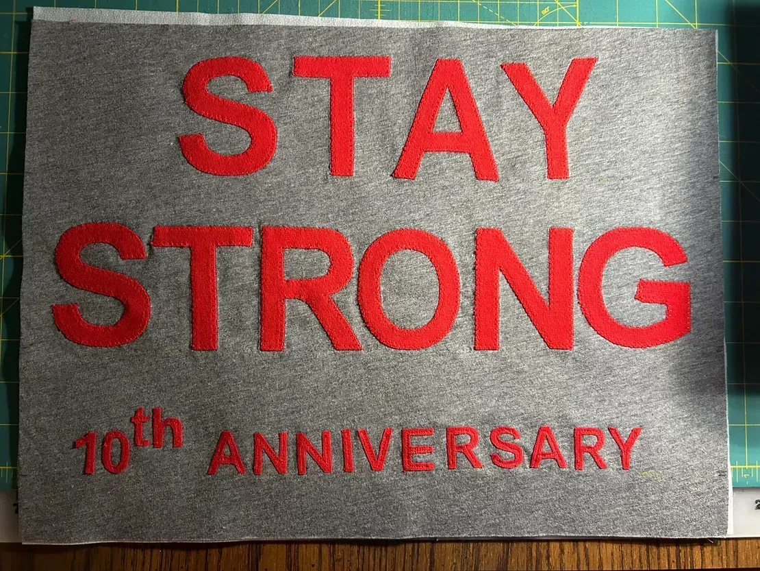 Red text embroidered on a grey felt patch reads: