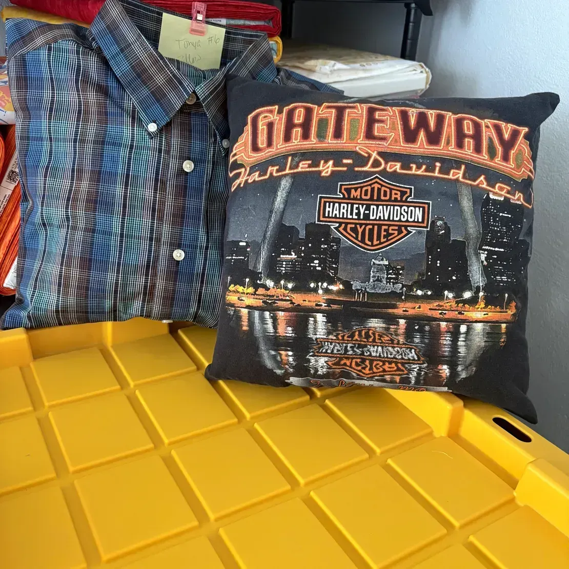 Two pillows on a yellow plastic bin: one with a blue-and-black striped button-down pattern and a Harley-Davidson graphic.