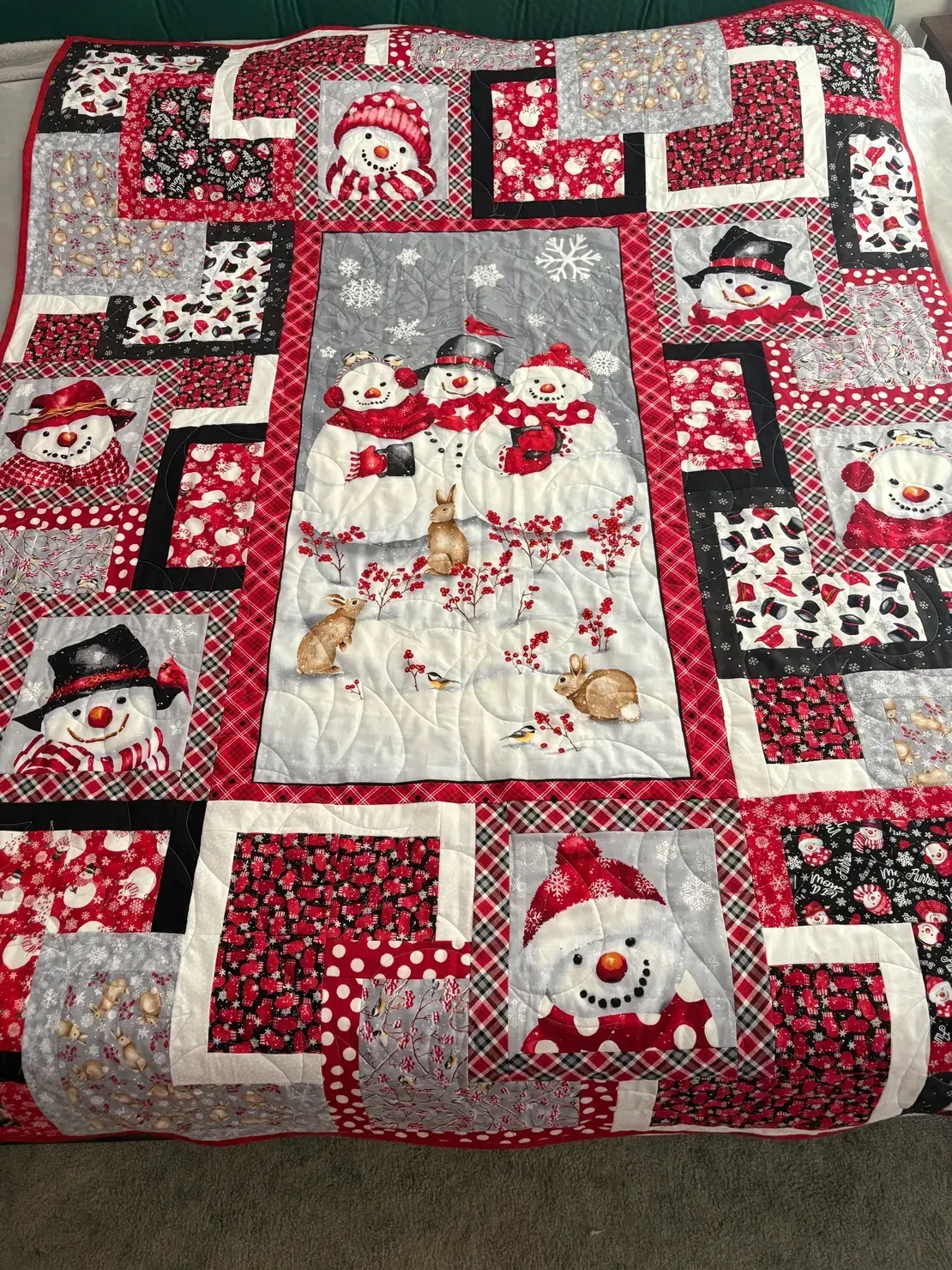 A patchwork quilt featuring various snowmen, red-and-black patterned fabrics, and a central scene of snowmen and rabbits.