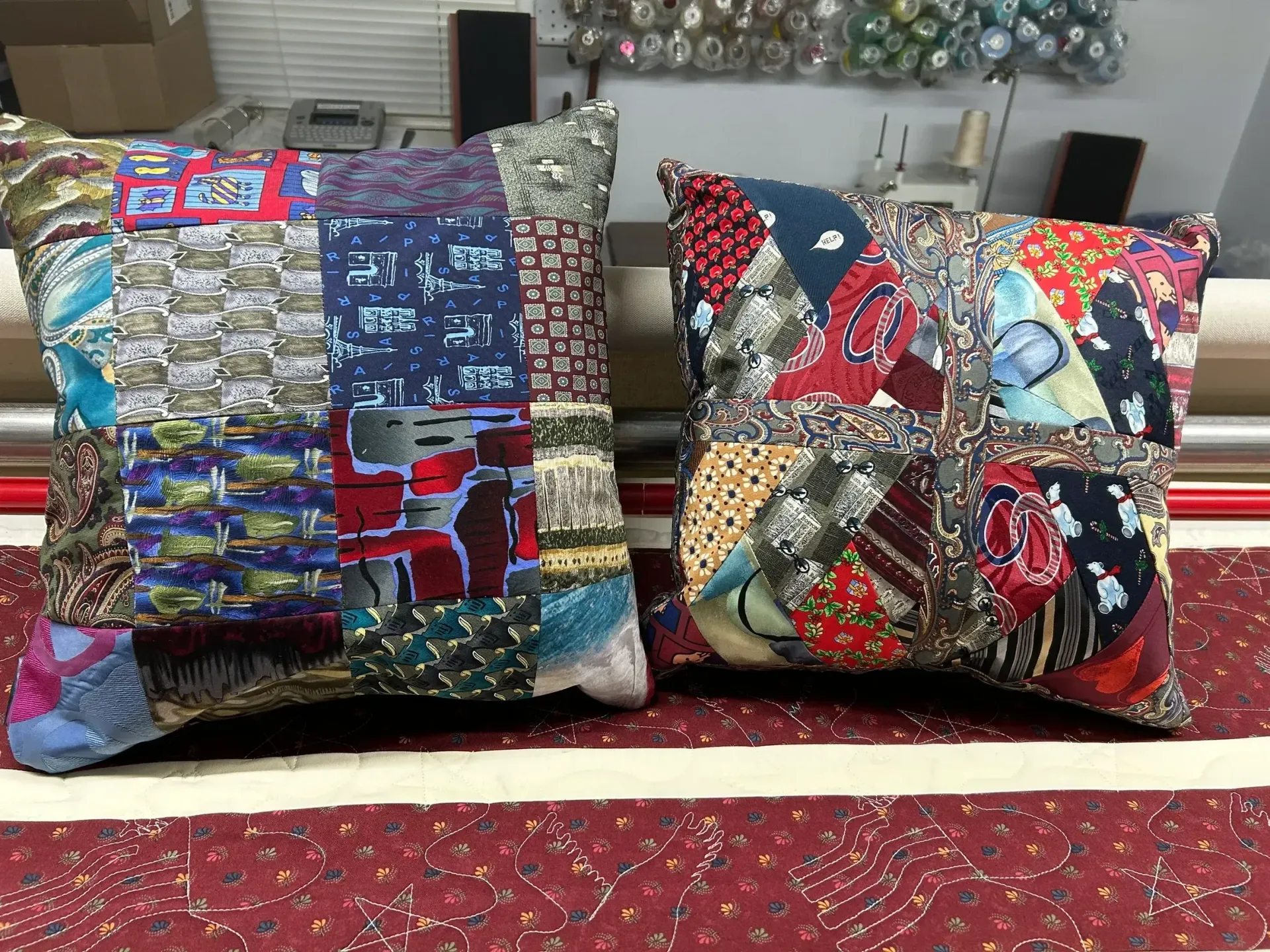 Two handmade patchwork pillows made from colorful patterned fabric scraps, resting on a red textured surface.